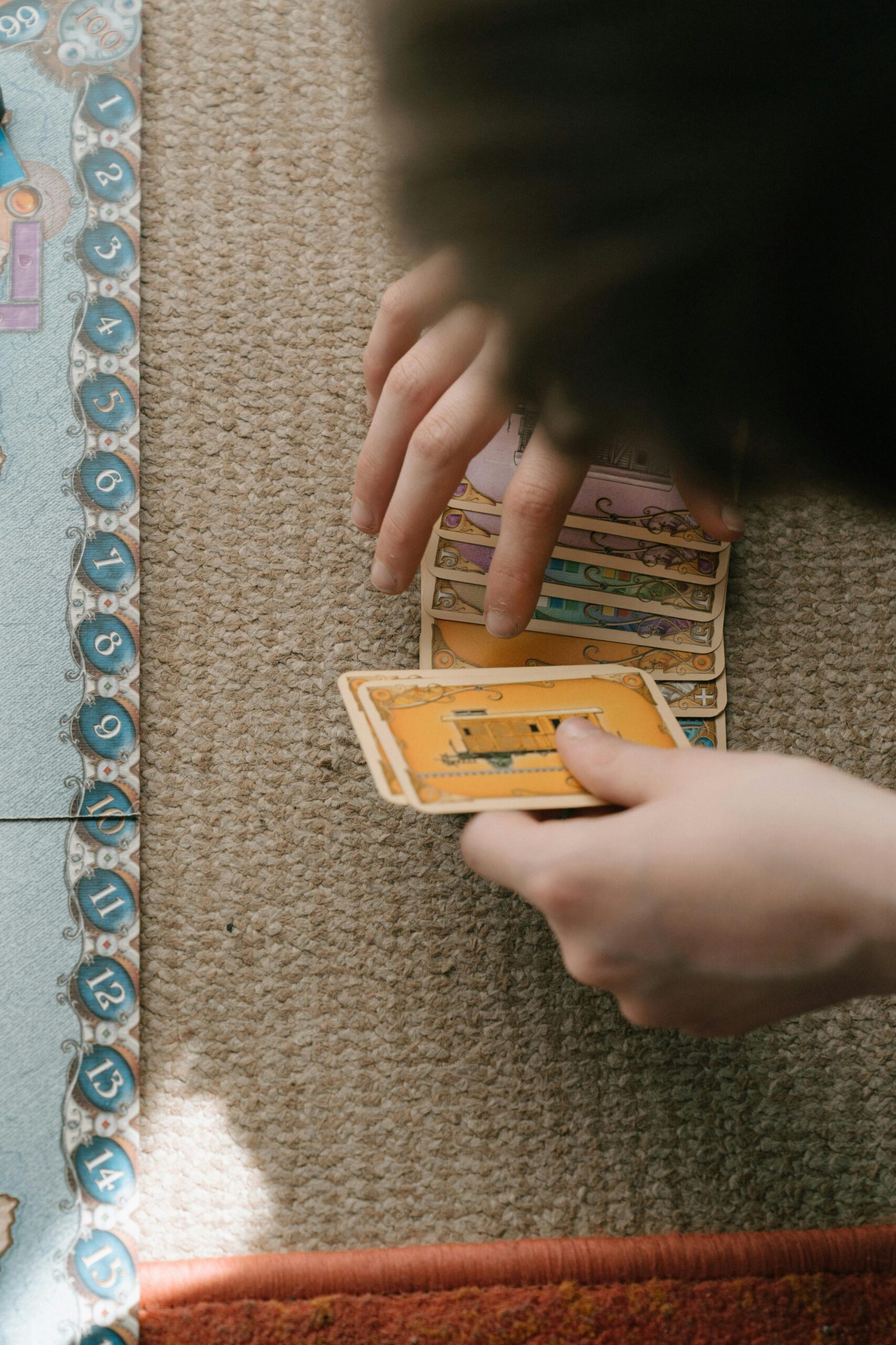 An overhead close-up shot of hands playing a strategic board and card game indoors.